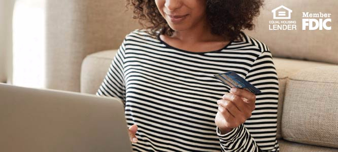 WOMAN HOLDING HER CREDIT CARD AND WORKING ON A COMPUTER