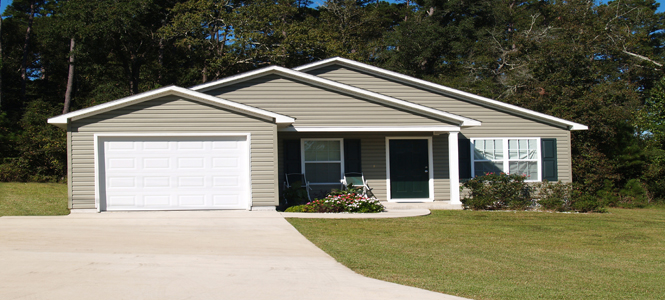 Small house with white garage door and tan siding.