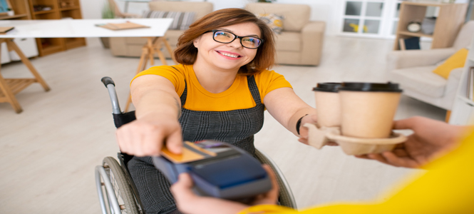 Young woman in wheelchair working in a coffee shop receiving payment with credit card machine.