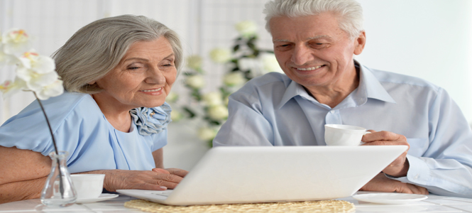 couple on a laptop, gray/white hair, white laptop, dressed in baby blue.